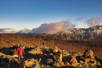Person wearing a red jacket standing in front of a vast, sun-drenched mountain landscape, UNESCO