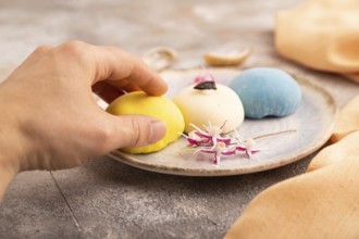 Japanese Mochi Cakes with hand on brown concrete background and orange textile, side view, close