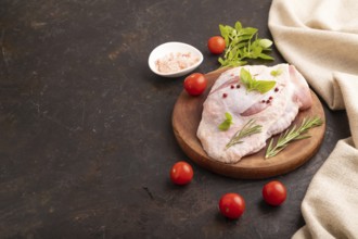 Raw Turkey Thigh with spices and rosemary on cutting board on black concrete background and linen