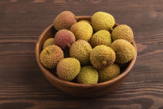 Ripe Lychee on clay bowl on brown wooden background, side view, close up, minimalism