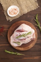 Raw Turkey Thigh with spices and rosemary on cutting board on brown wooden background and linen