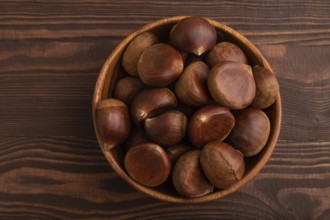 Wooden bowl with raw edible ?hestnuts on brown wooden background, top view, flat lay, close up,