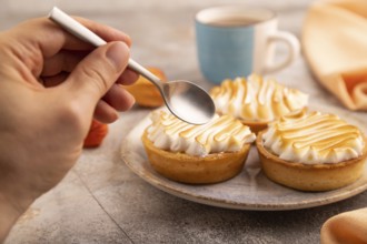 French lemon tart with meringue with hand on brown concrete background, cup of coffee, orange linen