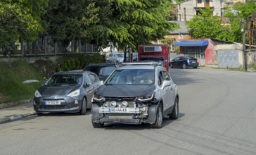 A damaged car drives on an urban road surrounded by trees and buildings, Georgia