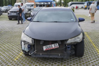 Dark car with frontal damage is parked in a parking lot with pedestrians, Georgia