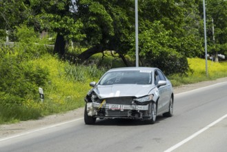 Silver car with frontal damage drives along a flower-lined road, Georgia