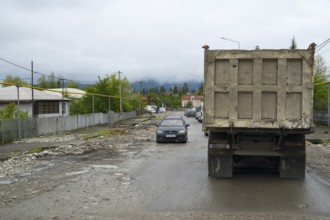 A truck and a car on a wet rural road with cloudy sky and mountains in the background, bad road in