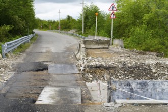 Partially closed road with signs and debris surrounded by green vegetation, bridge over the Techuri