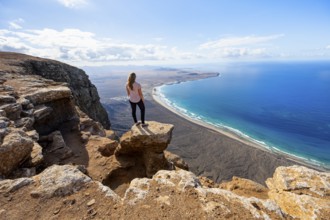 Young woman enjoying the view from the Risco de Famara cliffs to Famara beach, Playa de Famara with