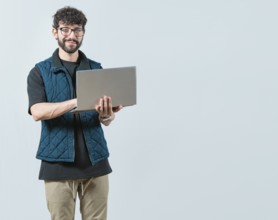 Smiling Bearded guy using laptop and looking at camera isolated. Handsome young man with glasses