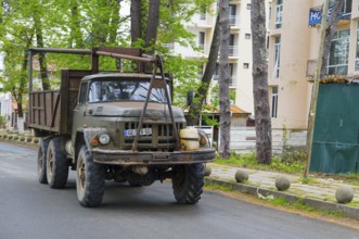 An old rustic truck is parked on a road next to tall buildings, truck ZIL -131, Ureki, Guria