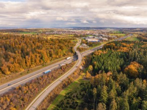 Road through autumn forest landscape with view of city in the distance and cloudy sky, A8 near