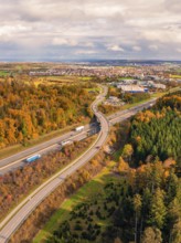 Aerial view of a road in autumn landscape with view of city and wooded area, A8 near Rutesheim,
