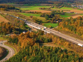 Road with bridge through autumn landscape with green fields and wooded hills, A8 near Rutesheim,