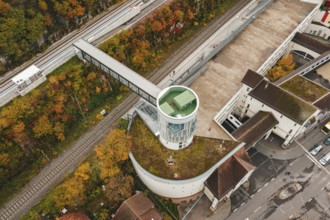 View of tower next to train tracks and parking lot, surrounded by autumn colors, Hermann Hessebahn,