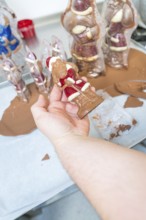 A hand holds a chocolate Santa Claus figure in a production environment, Christmas baking,
