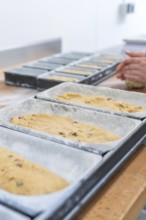 Dough in loaf pans, hands of a baker working dough in the background, Christmas baking,
