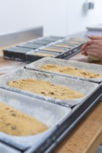 Close-up of dough in loaf pans, hands of a baker visible in the background, Christmas baking,