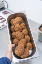 One hand holds a rectangular metal bowl full of brown chocolate chocolates, Christmas baking,