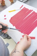 Hand cuts red paper strips with scissors on baking tray, Christmas baking, Haselstaller Hof,