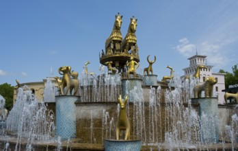A fountain with golden statues in front of urban architecture and sparkling water, golden horses,