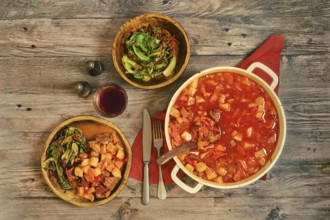A large pot of beef stew on a wooden tabletop. Portion of beef stew is served on a rustic wooden