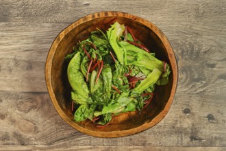 A wooden bowl filled with steamed greens on a rustic wooden tabletop. The leafy vegetables,