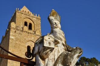 Stone statue of a saint in front of a tower against blue sky, symbolizing historical strength of