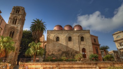 Side view of an Arab-Norman building with red domes and palm trees in sunny weather, Palermo, San
