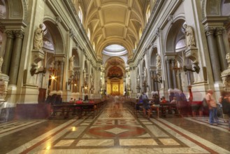Magnificent church interior with high vaults and sculptures, enlivened by lights and visitors,