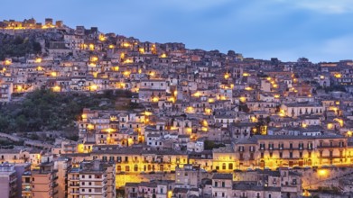 Modica, evening view of a mountainous urban landscape with illuminated houses, Baroque towns of