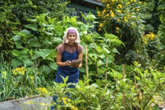 Senior woman gardener in an apron writing notes in a small book, observing healthy plants growing