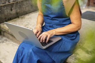 Senior woman on concrete steps typing on laptop outdoors, enjoying flexible remote work and modern
