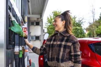 Woman smiling at a gas station while holding a fuel pump nozzle beside her red car in a plaid