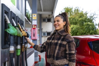Woman smiling and wearing a protective glove while selecting a fuel pump to refuel her red car at a