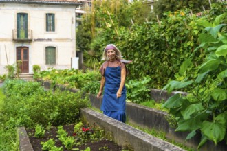 Senior woman smiling while walking through her bountiful urban vegetable garden, cultivating fresh