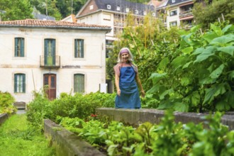 Woman gardener smiling while standing in a lush, rustic raised bed vegetable garden, cultivating