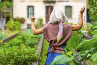 Senior woman with gray hair and a colorful scarf enjoying a sunny day outdoors, raising her arms in