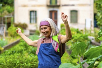 Happy senior woman dancing with arms raised in her home garden, celebrating an active and joyful