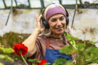 Senior woman wearing headphones and an apron, smiling happily while listening to music and working