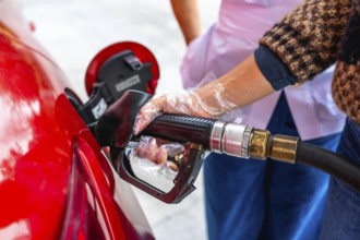 Person is refueling a red car at a gas station, holding a fuel pump nozzle with a protective