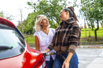 Mother smiling as daughter fills the red car with fuel at a gas station, sharing a warm moment of