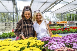 Happy mother and adult daughter enjoying choosing colorful blooming flowers together, bonding and