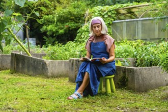 Senior woman wearing an apron and headband, enjoying a quiet moment reading a book while sitting on