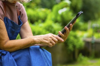Senior woman is holding and interacting with a digital tablet in a vibrant green garden, embracing
