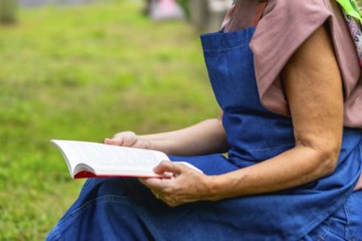Senior woman sitting in a sunny park, calmly reading a book and enjoying peaceful outdoor leisure