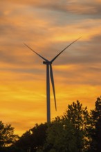Stationary wind turbine, wind turbine, rotor blades and generator, silhouette, atmospheric sky in