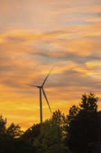 Stationary wind turbine, wind turbine, rotor blades and generator, silhouette, atmospheric sky in