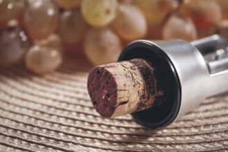 A corkscrew with a wine bottle stopper, lying on a woven napkin, with green grapes