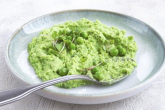 A vibrant green pea puree fills a shallow bowl, topped with fresh peas and microgreens. The dish